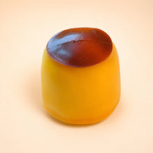 Studio real product photo of the NOLLUMI Caramel Pudding Squishy, centered on a warm ivory and pale peach background