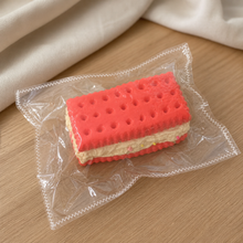 Real product photo of the NOLLUMI Dopamine Sandwich Cookie Squishy in its clear sealed wrapper on a warm neutral setting
