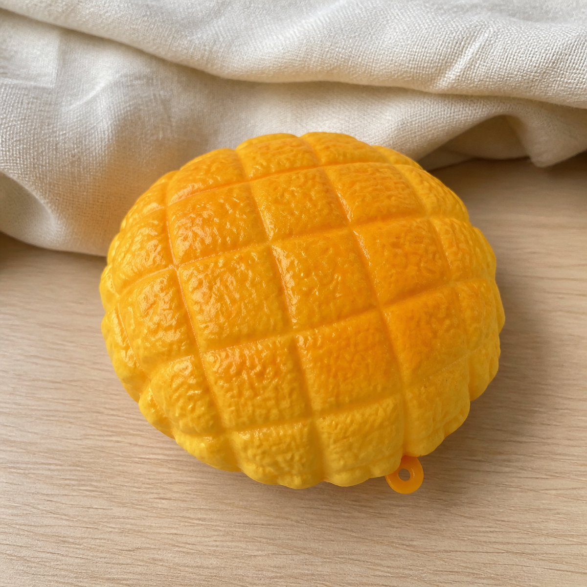 Real product photo of the NOLLUMI Golden Bun Squishy with hanging loop on a warm neutral setting