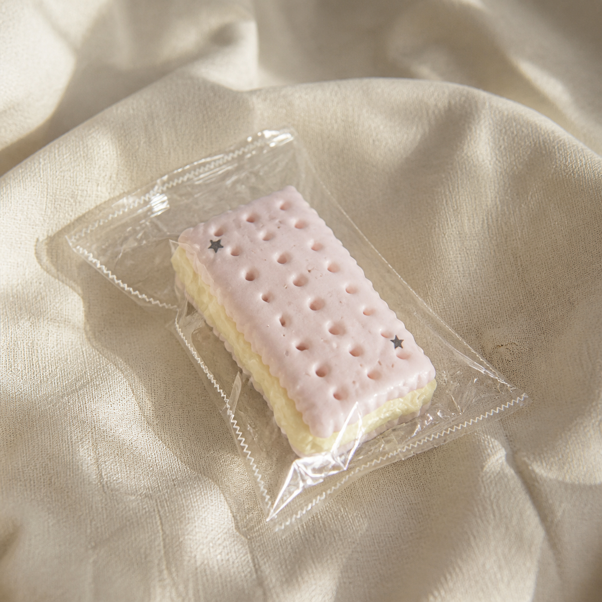 Real product photo of the NOLLUMI Macaron Sandwich Cookie Squishy in its clear sealed wrapper on a warm neutral setting